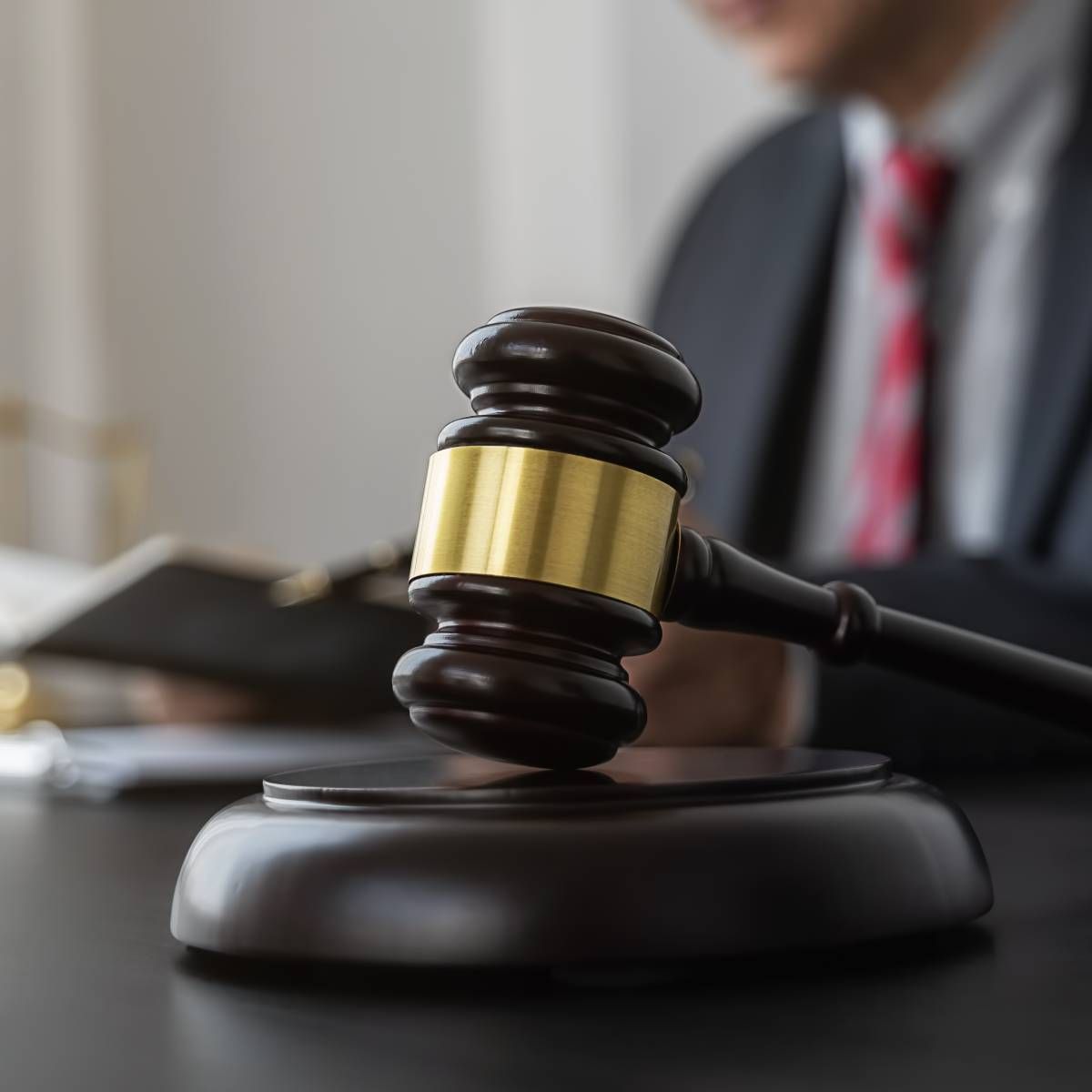 Wooden gavel on a stand; a person in a suit is blurred in the background.