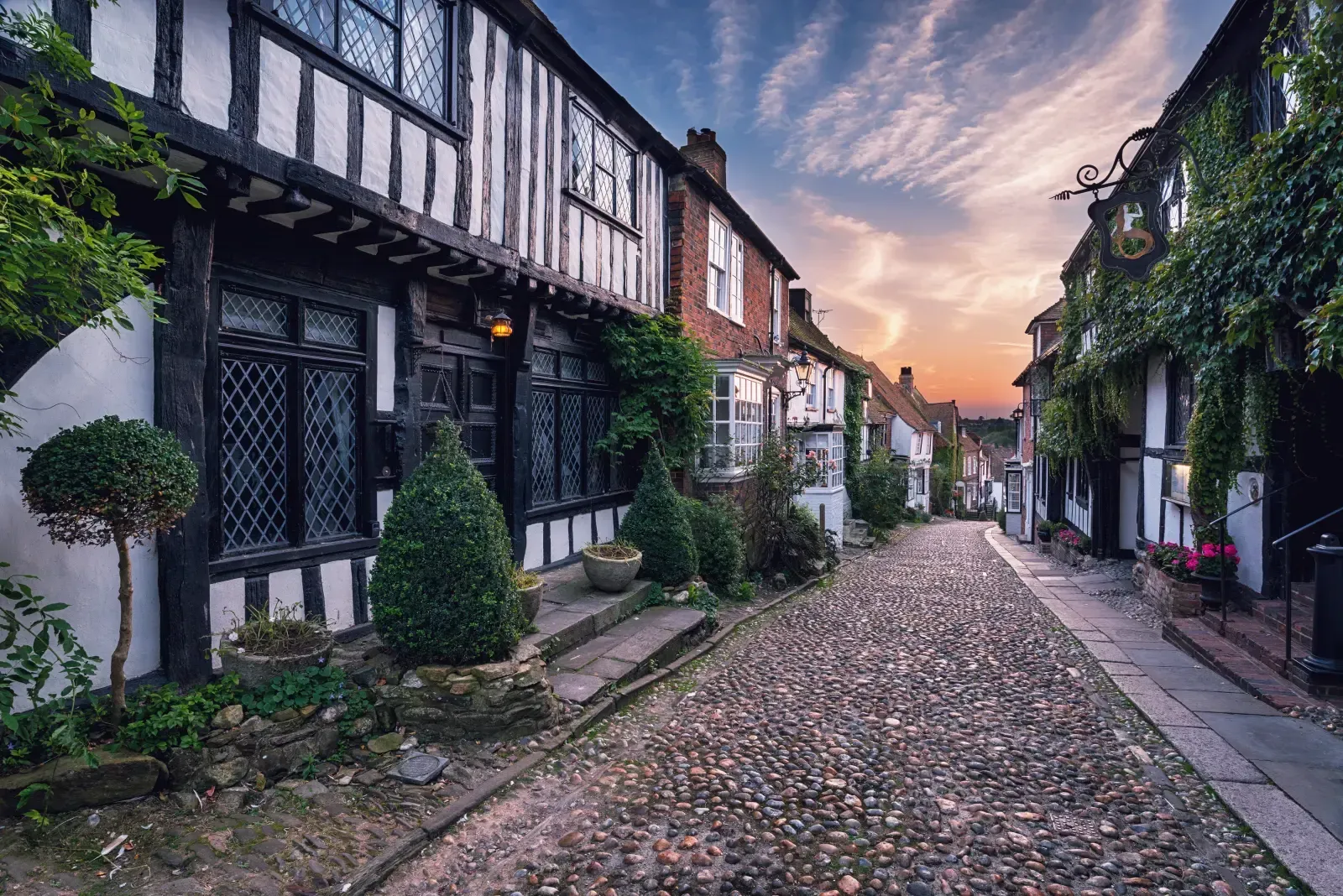 A narrow, cobblestone street lined with historic timber-framed buildings during a colorful sunset.