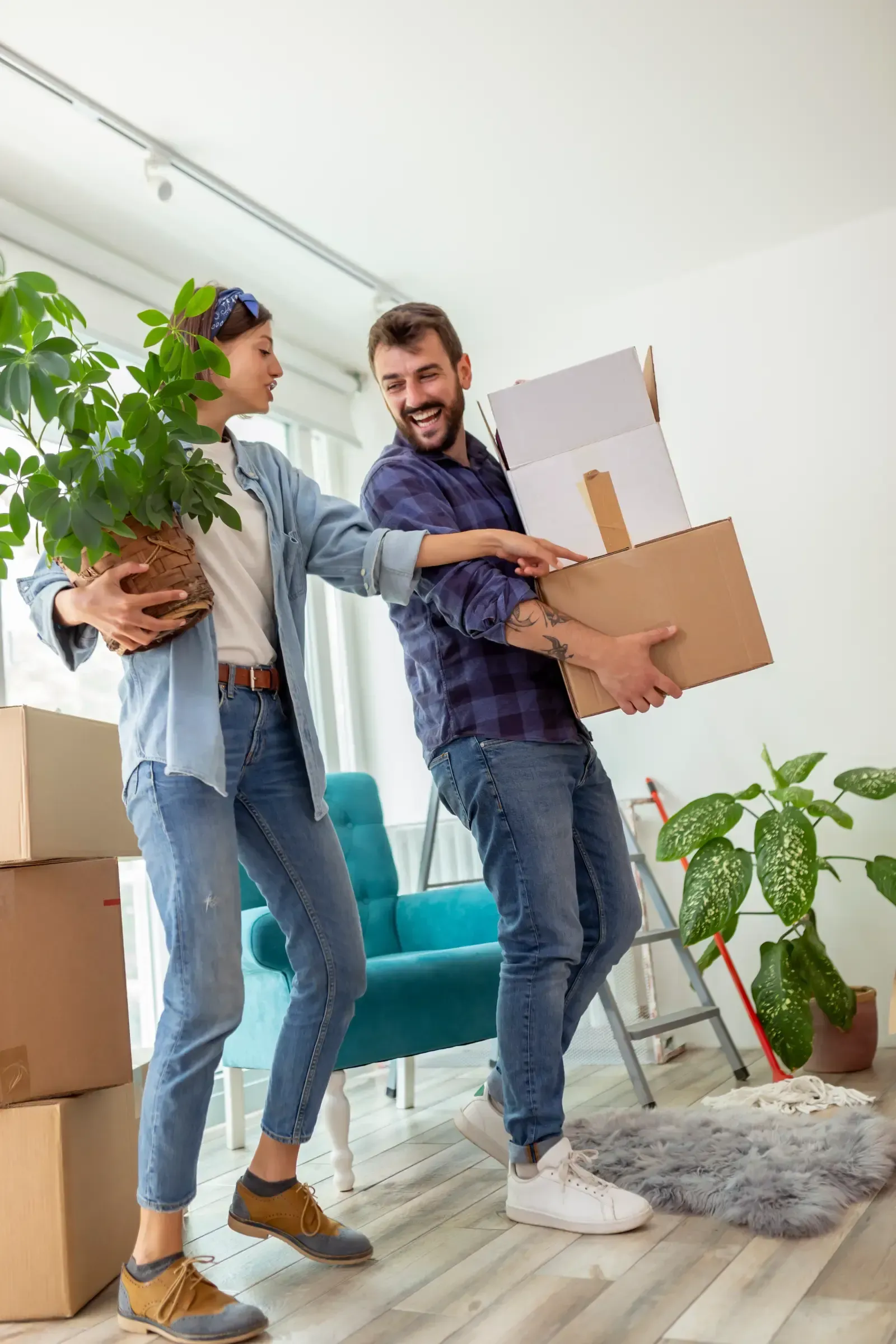 Couple carrying boxes and a plant while moving into a new home.