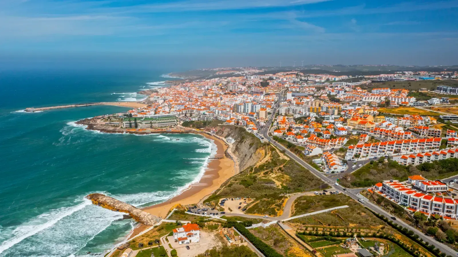 Aerial view of a coastal town in Portugal, featuring white buildings with orange roofs along a sandy beach and blue ocean.