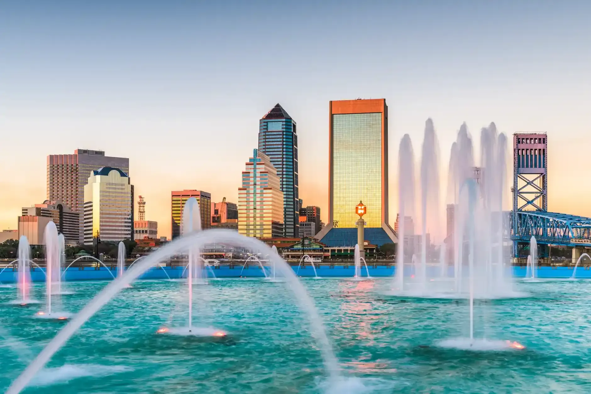 Jacksonville, FL skyline with fountains arcing over turquoise water at sunset