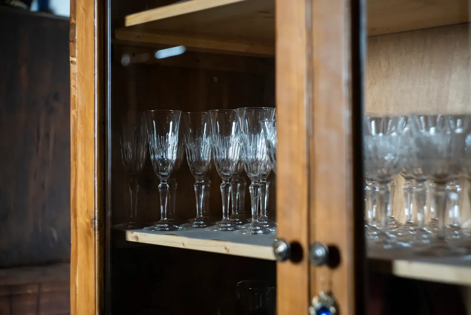 Crystal wine glasses inside a wooden cabinet with glass doors.