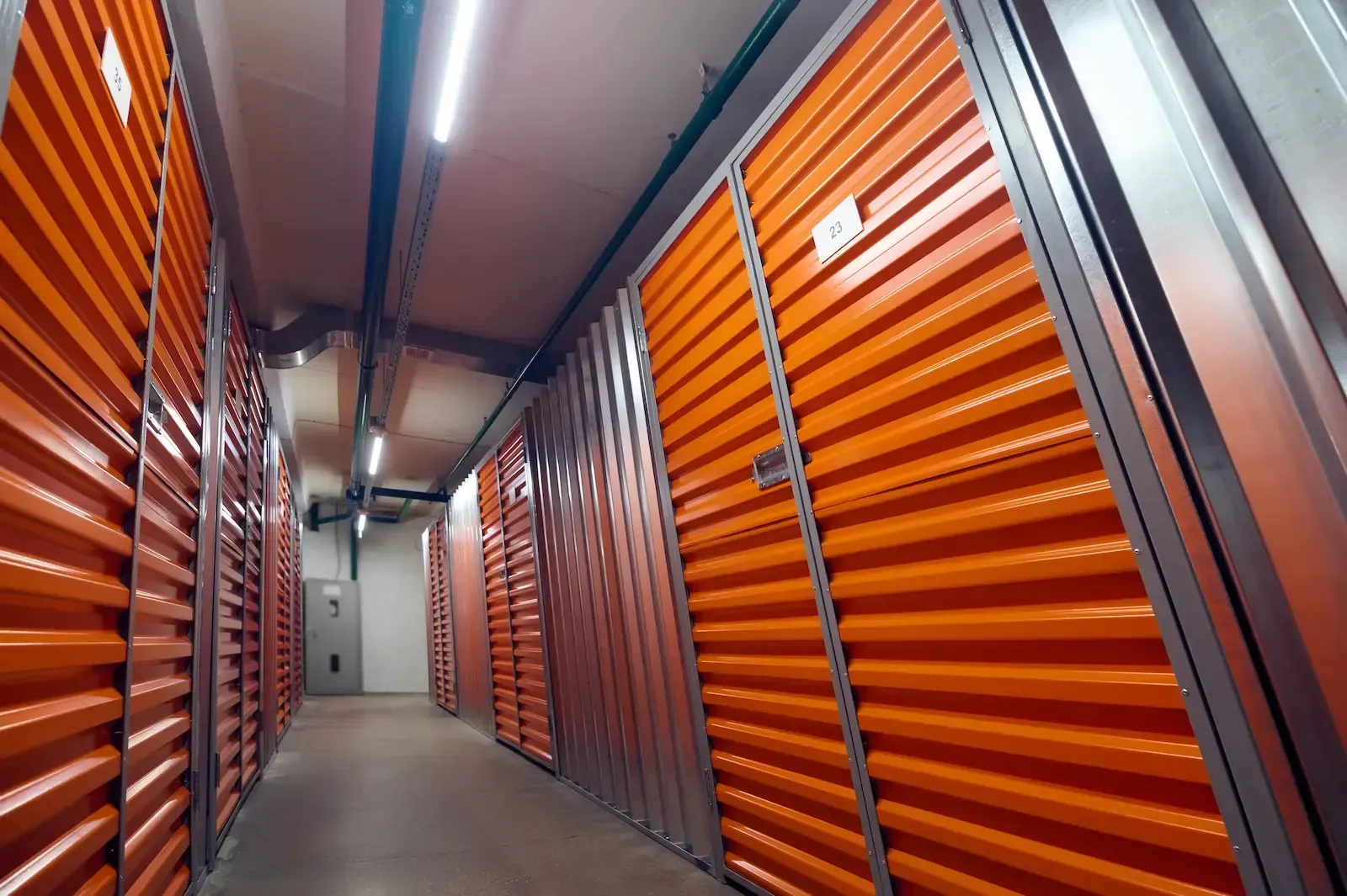Interior of a storage facility with rows of orange storage units, a long hallway, and overhead lighting.