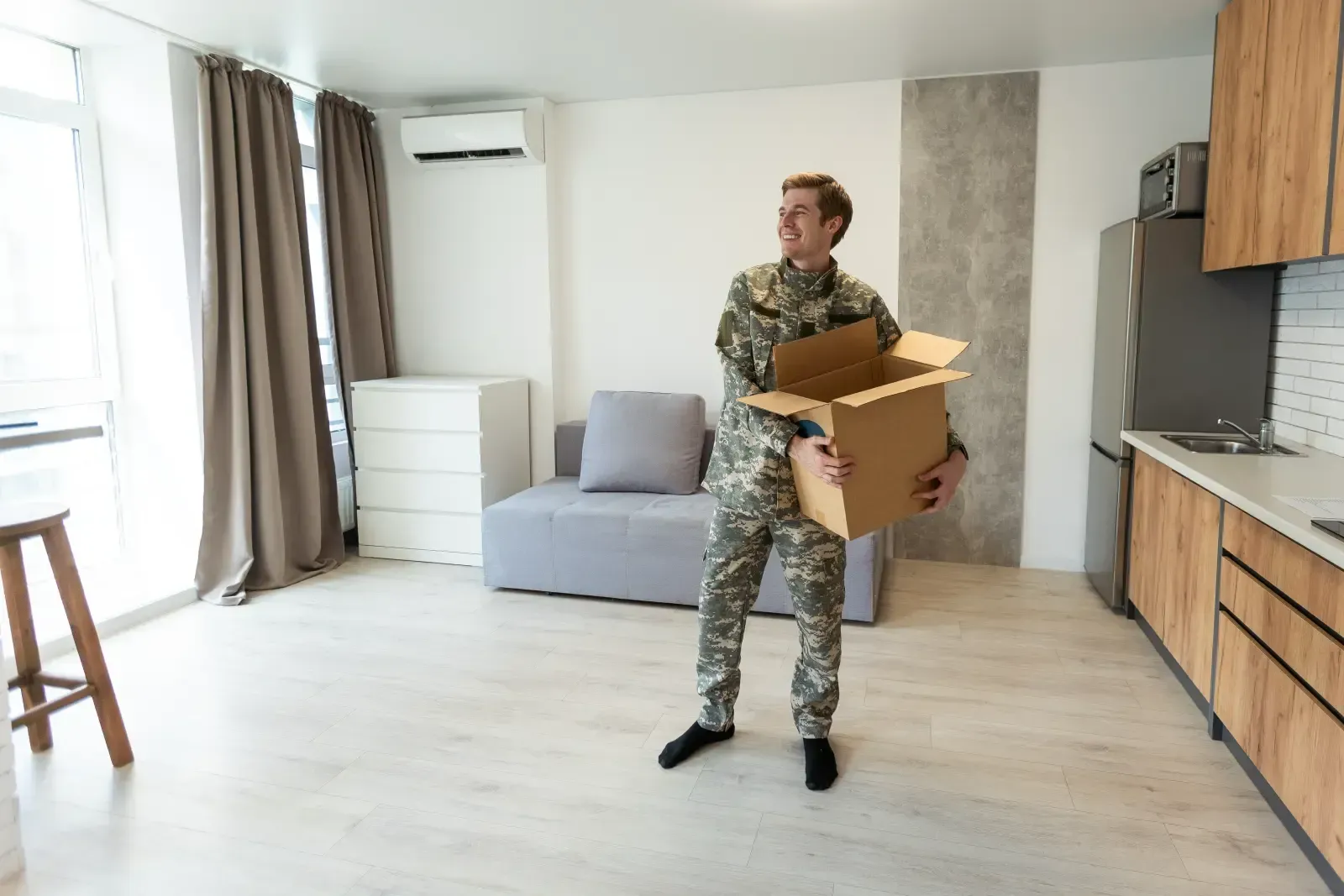 Man in camouflage holding an open box in a new apartment.