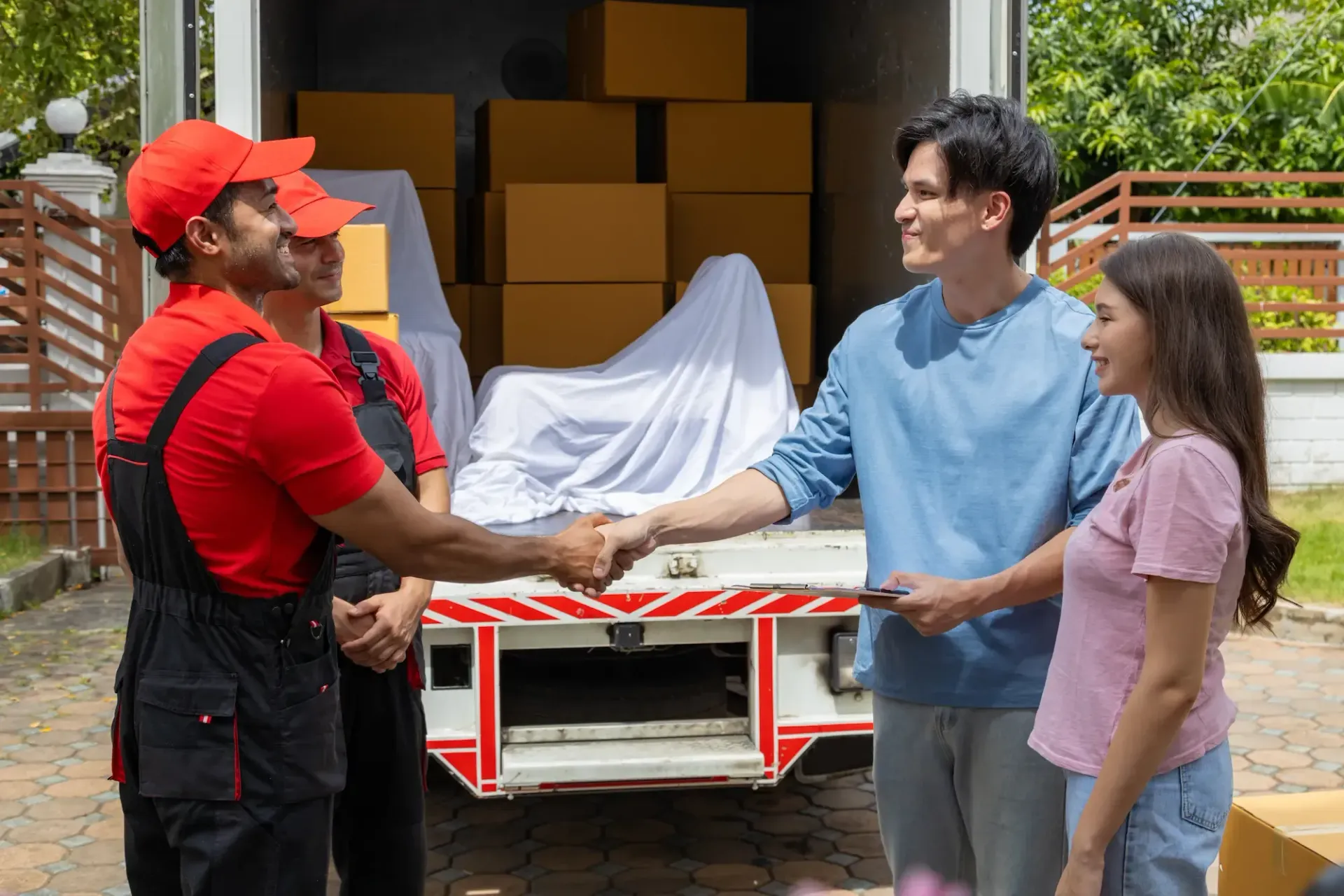 Young couple checks with two movers unloading boxes and furniture from a pickup truck