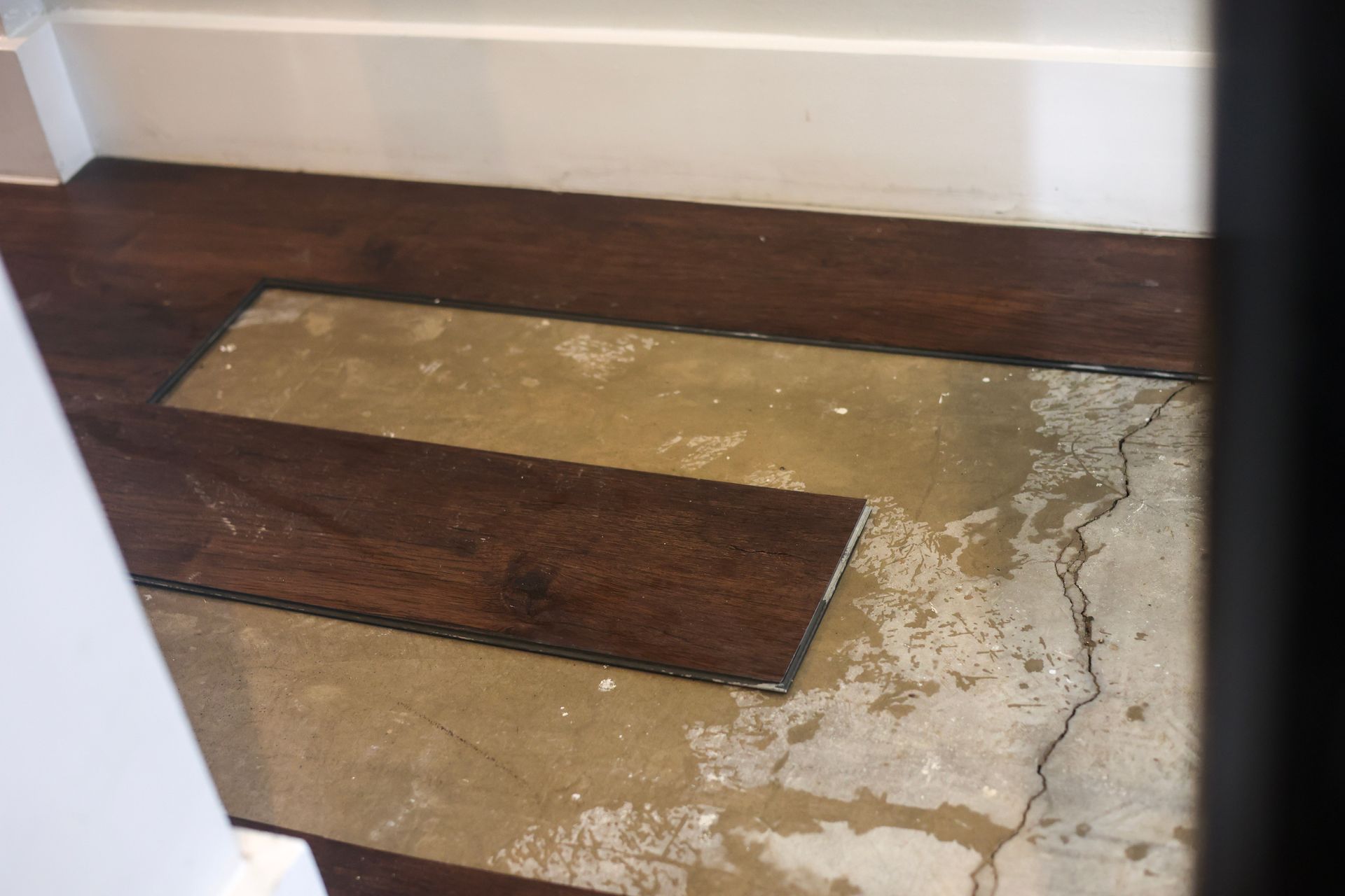 Dark wood flooring partially installed on a concrete surface, with a gap in the center and cracks visible.