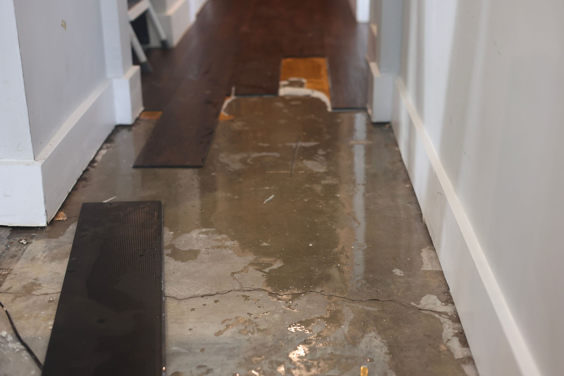 Hallway with damaged concrete floor and scattered wood planks. Water and debris are present.