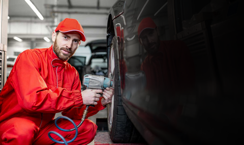 Two men in red uniforms are holding tires and giving a thumbs up.