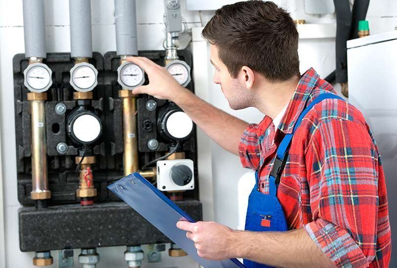 A Man in a Plaid Shirt is Working on a Heating System While Holding a Clipboard — FNQ Hot Water In Mareeba, QLD