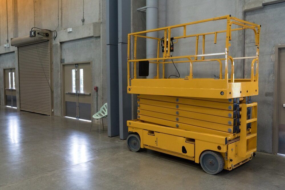 A Yellow Scissor Lift is Parked in an Empty Warehouse — FNQ Hot Water In Mareeba, QLD