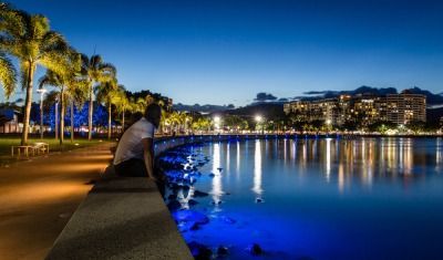 A Man is Sitting on a Pier Overlooking a Body of Water at Night — FNQ Hot Water In Cairns, QLD