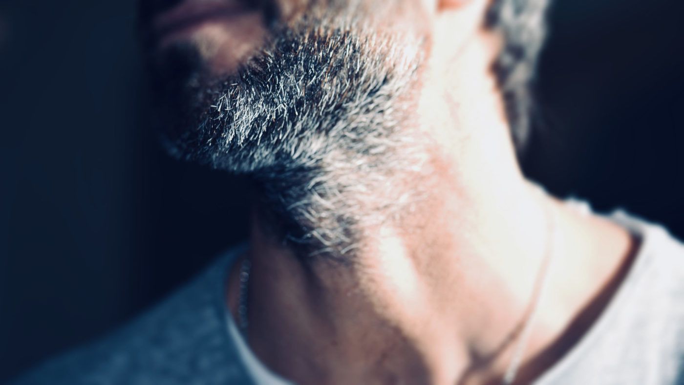 Close-up of a person's neck and jawline, showing a graying beard and a plain t-shirt.