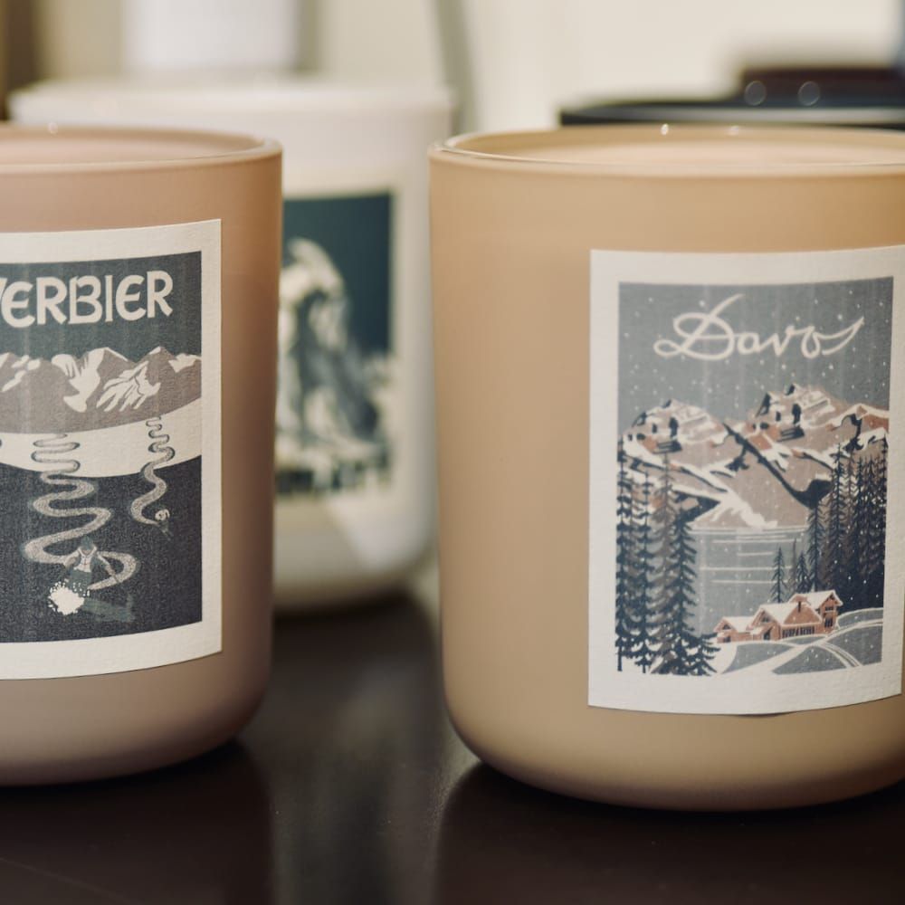 Trois bougies en verre dépoli avec des étiquettes de scènes de montagne de style vintage : Verbier, Davos et une troisième.