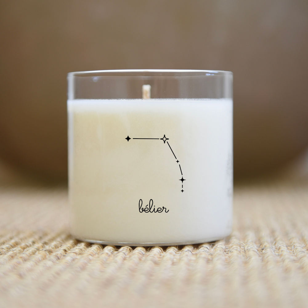 Bougie dans un pot en verre ornée du symbole « Bélier » et de la constellation du Bélier. Posée sur une surface tissée.