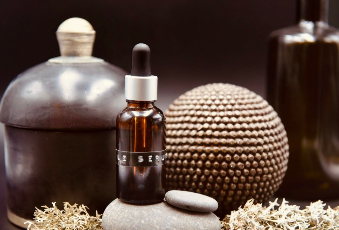 Flacon ambré avec compte-gouttes sur pierre grise ; sphères décoratives et poteries sur fond sombre.