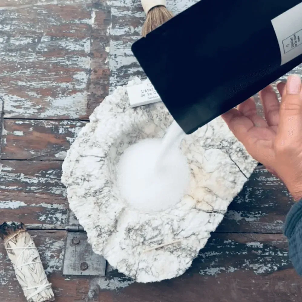 Personne versant de la poudre blanche d'une poche noire dans un bol en pierre, sur une surface en bois.