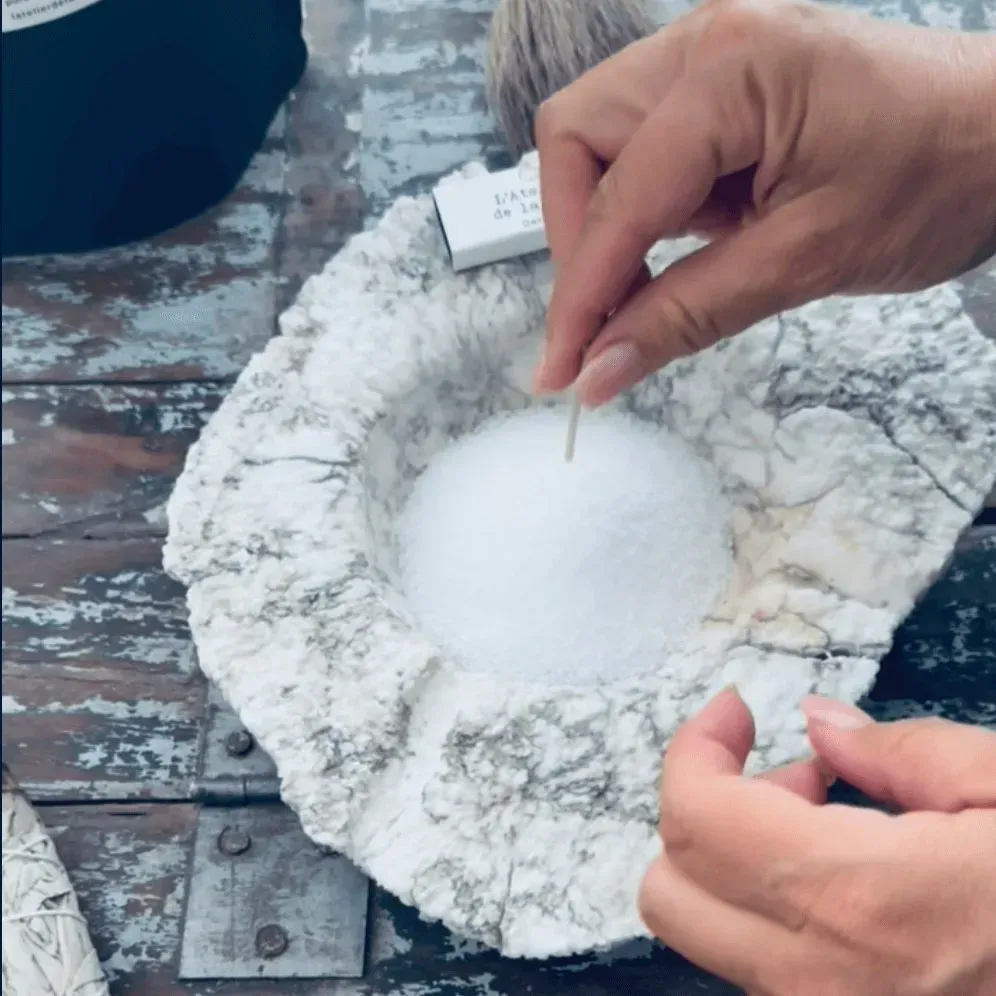 Mains tenant un cure-dent au-dessus d'un bol de sel blanc dans un récipient semblable à du marbre.