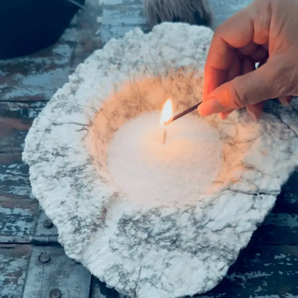 Allumage manuel d'une bougie dans un bol blanc texturé. Surface en bois, vue de dessus.