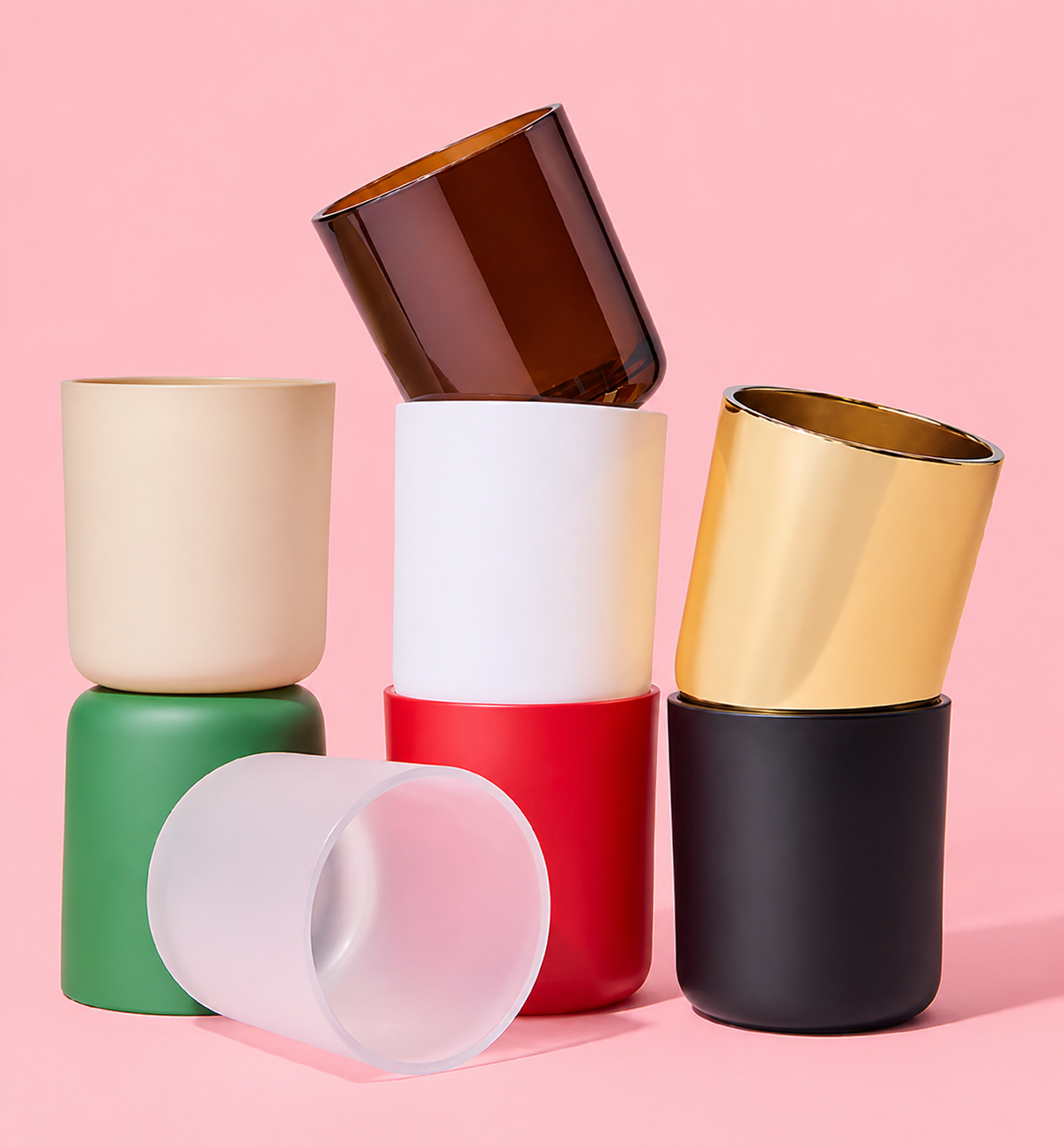Des tasses colorées empilées sur un fond rose, avec une tasse blanche couchée sur le côté.
