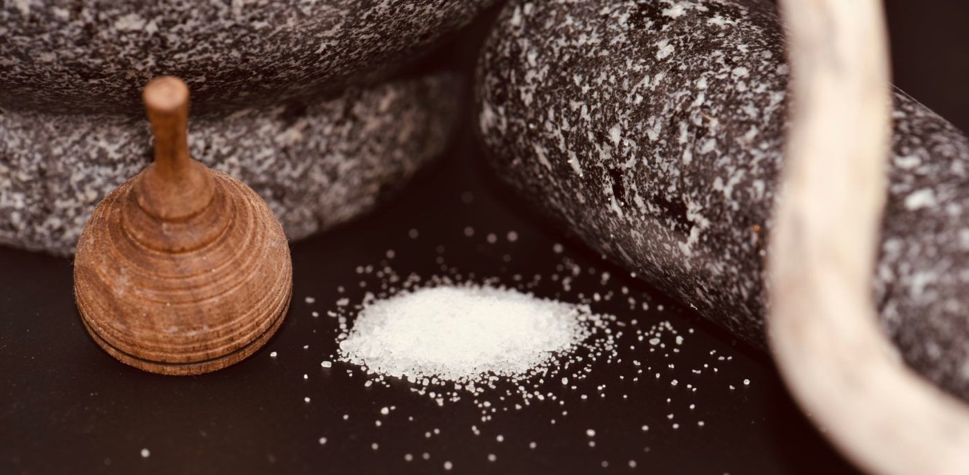 A wooden top, salt, and dark stones on a black surface.