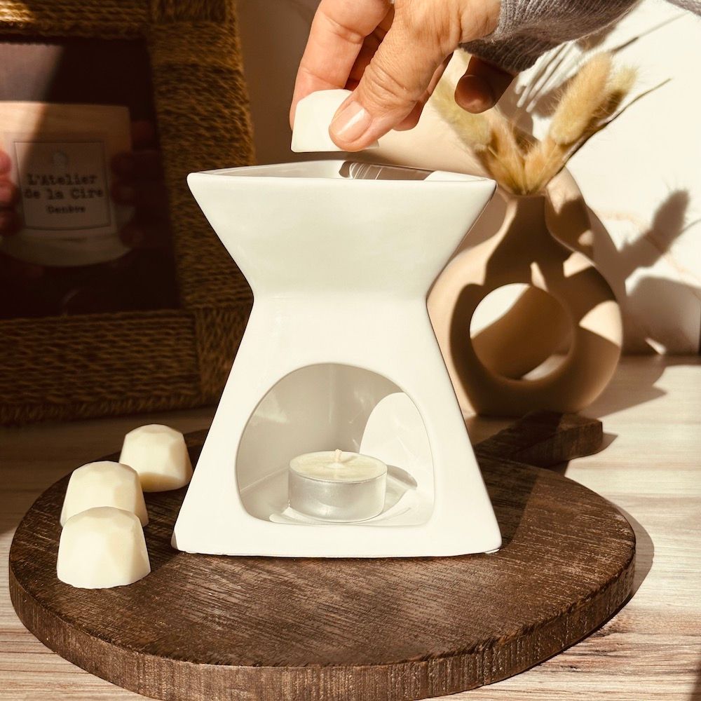 Placer à la main un fondant de cire dans un réchaud en céramique blanc avec une bougie chauffe-plat allumée. Base en bois avec fondants de cire.