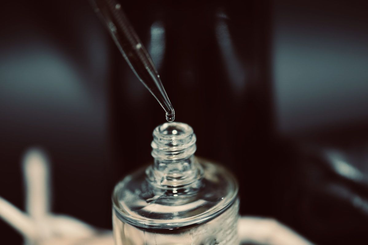 Dropper dispensing liquid into a small, open glass bottle.