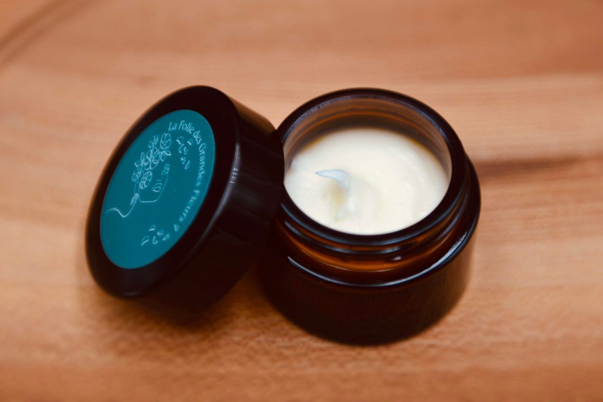 Small open jar of cream with its teal-labeled cap next to it, on a wooden surface.