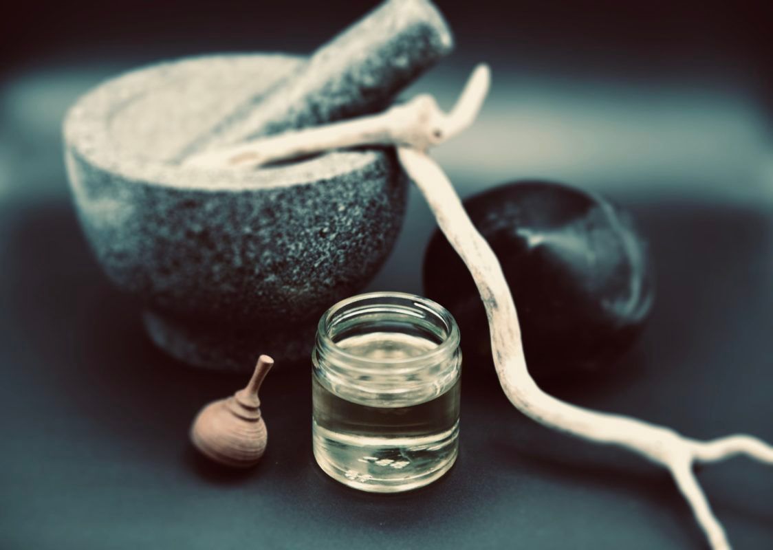 A mortar and pestle with small jar of liquid, wooden artifact on dark surface.