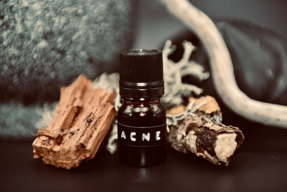 Bottle of acne treatment with “ACNE” on it, surrounded by wood, rock, and a white branch.