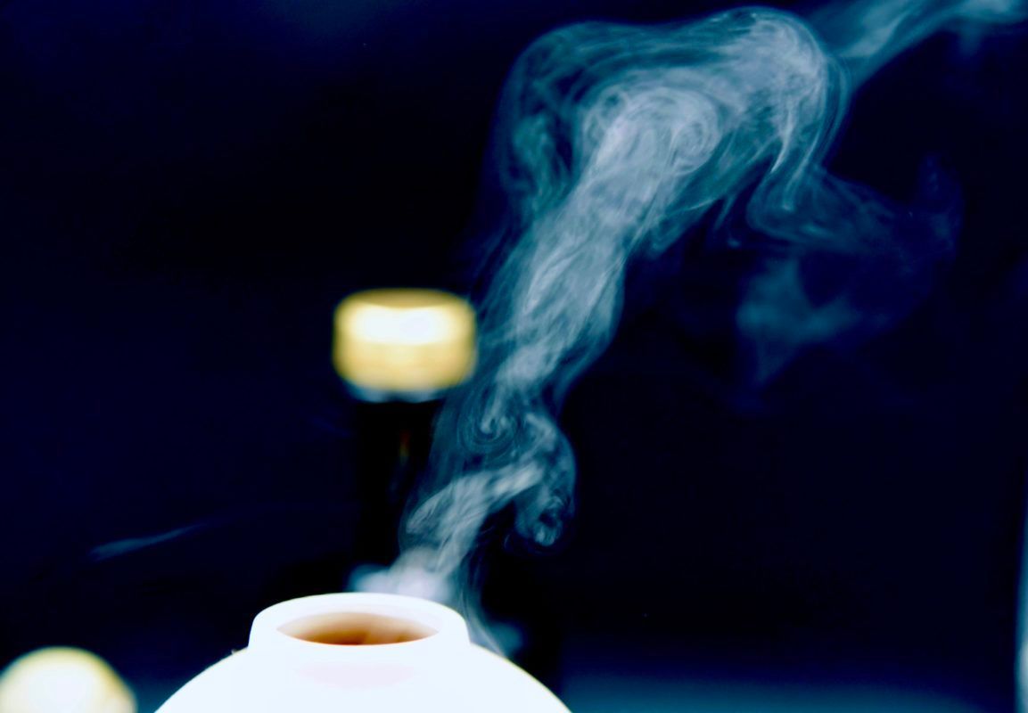 White ceramic vessel emitting wisps of light blue smoke, against a dark blue background.
