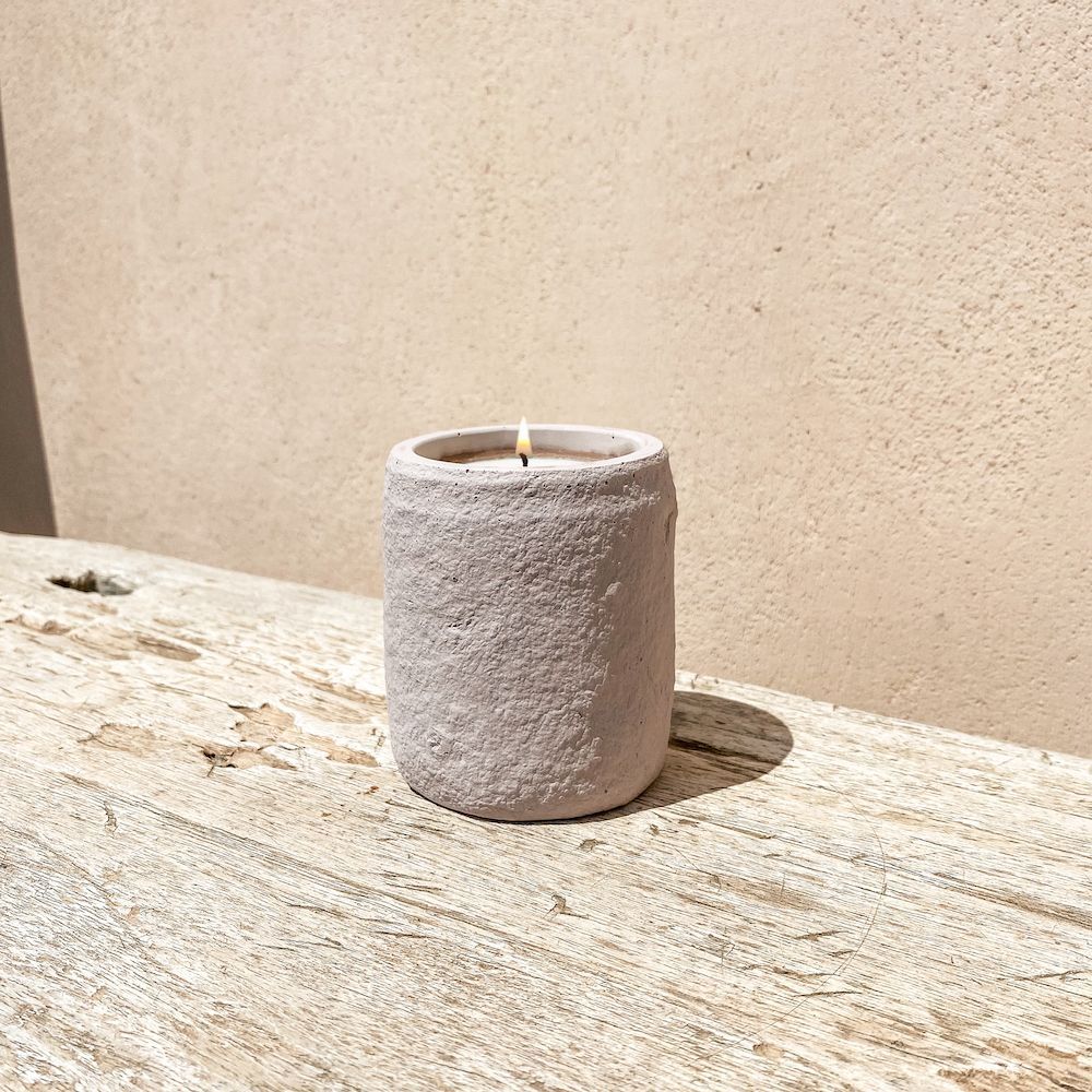 Bougie allumée dans un récipient cylindrique texturé rose clair sur une surface en bois patinée.
