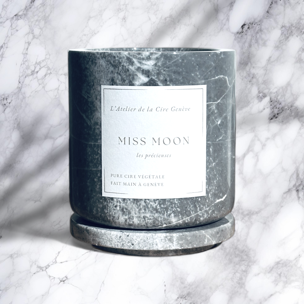Bougie en marbre gris étiquetée « Miss Moon » sur une soucoupe assortie, sur un fond en marbre.