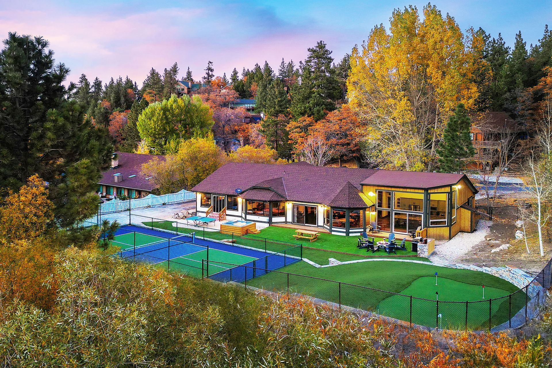 An aerial view of a house with a tennis court and a putting green surrounded by trees.