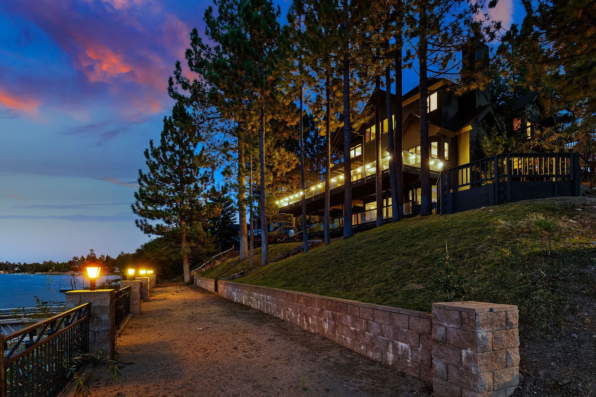 A large house sits on a hill overlooking a lake at night.