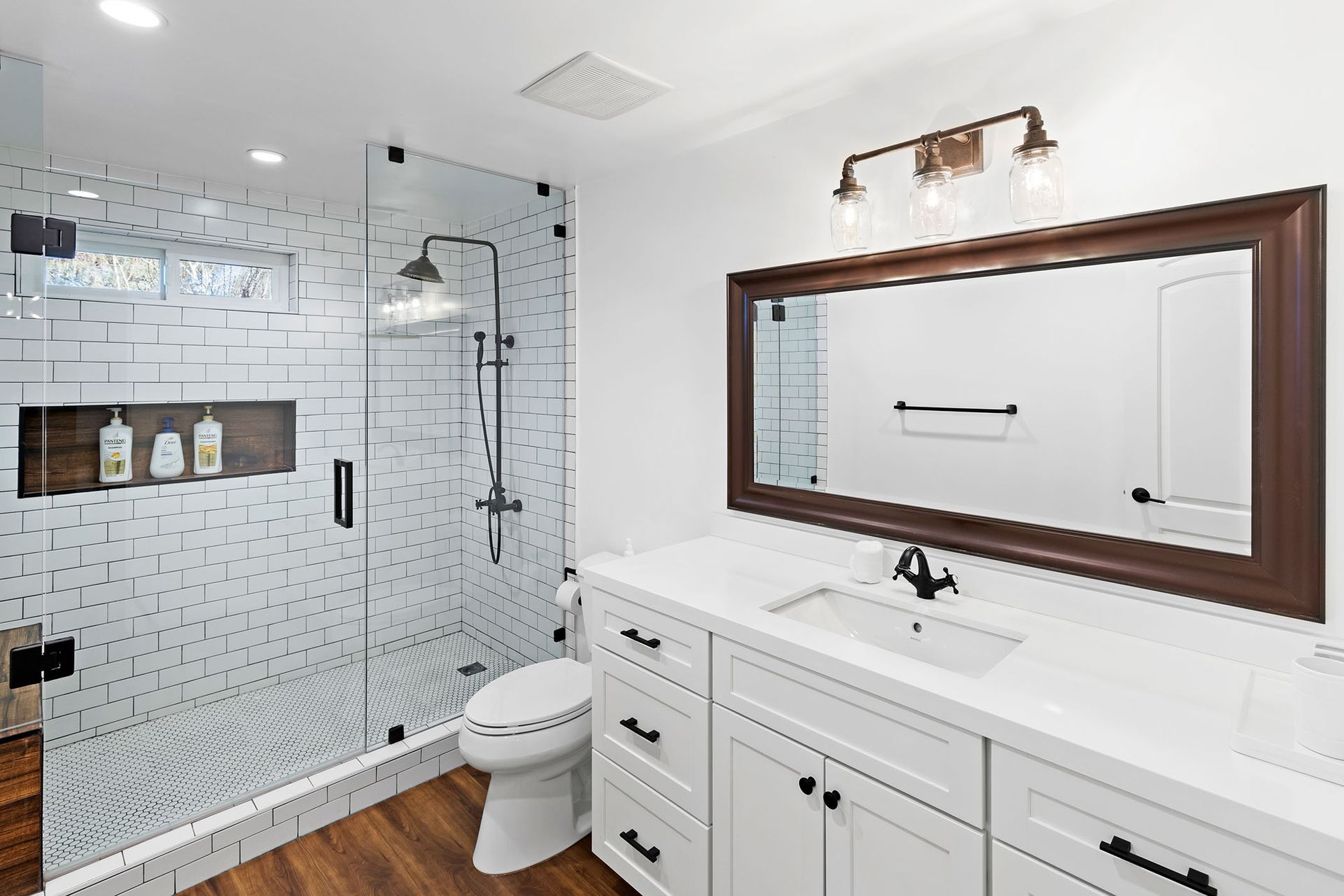 A bathroom with a toilet , sink , mirror and walk in shower.