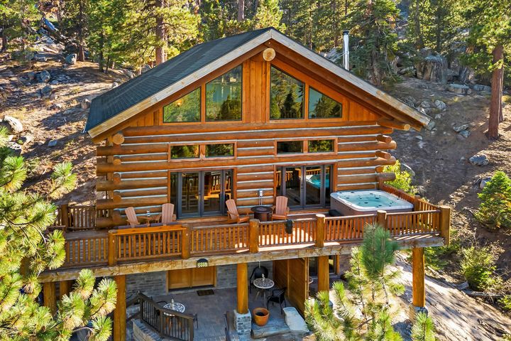 An aerial view of a log cabin with a hot tub on the deck surrounded by trees.