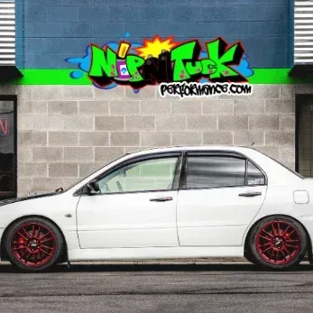 A white car is parked in front of nip n tuck performance shop