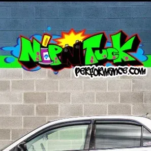 A car is parked in front of a brick wall with graffiti on it