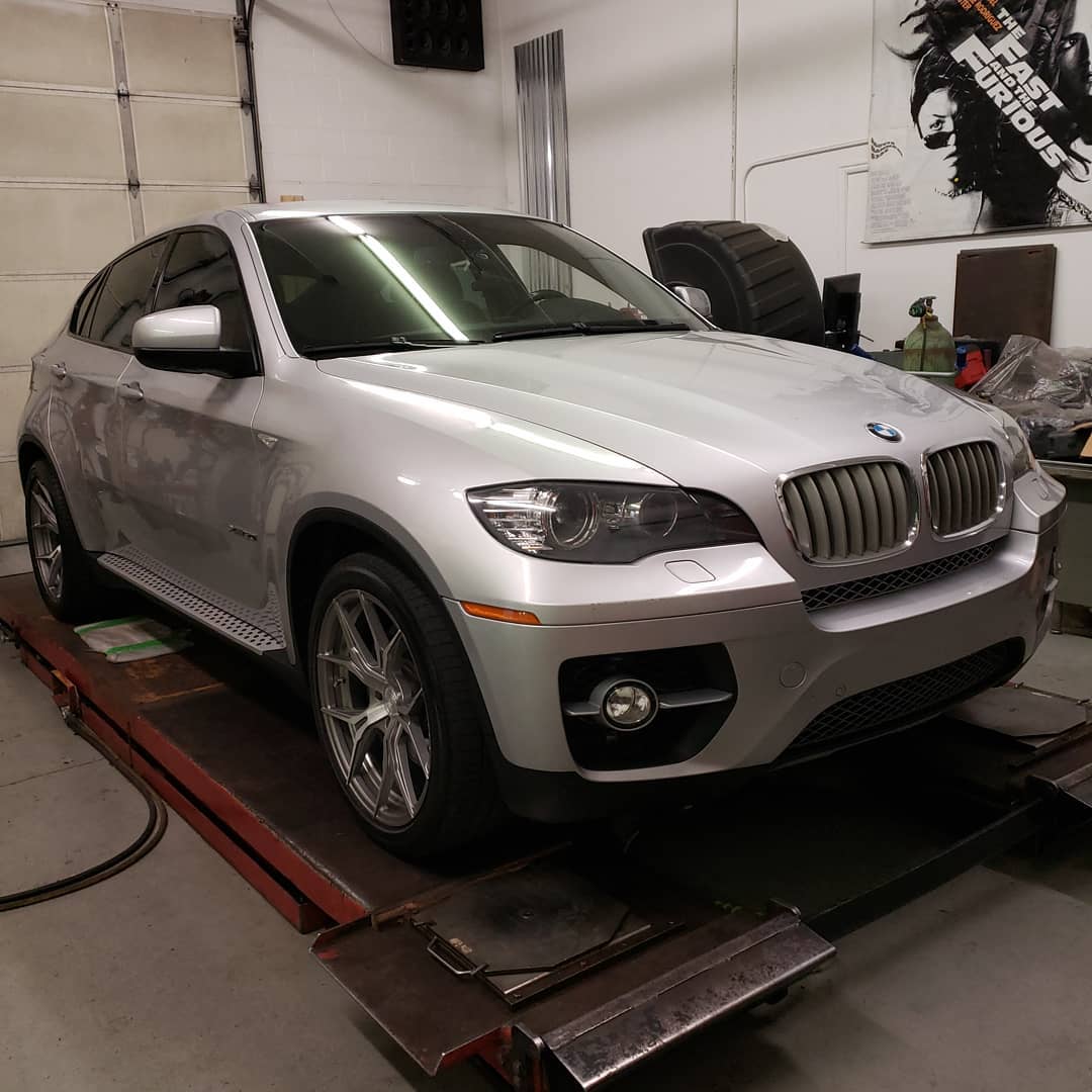 A silver bmw is on a lift in a garage
