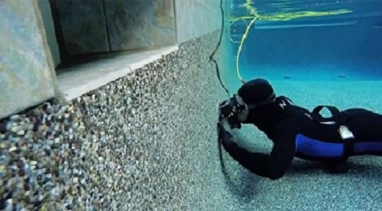 A scuba diver is taking a picture of a wall in a pool.