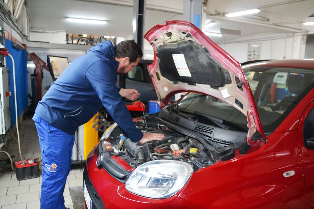 Un meccanico ispeziona un'auto rossa con il cofano aperto in un'officina meccanica.