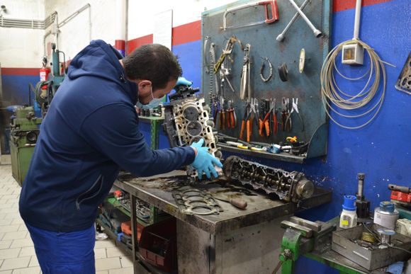 Un meccanico Autofficina e Centro Revisioni Lombardo Giuseppe - Meccanico Palermo lavora su un motore in un'officina, con gli attrezzi appoggiati su una rastrelliera a muro.