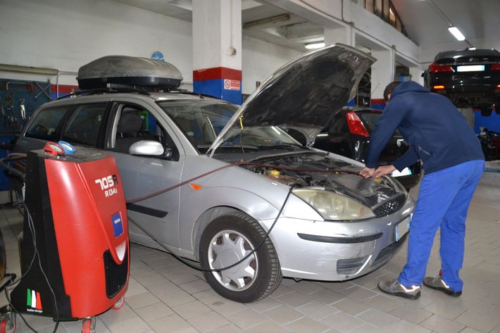 Un meccanico ispeziona un'auto argentata con il cofano aperto in un'officina meccanica.