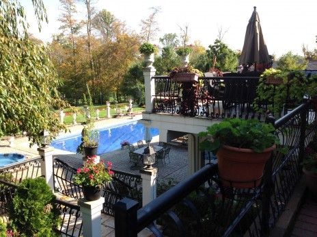 An elevated view of a backyard featuring a swimming pool, patio dining area, and a deck with potted plants and furniture.