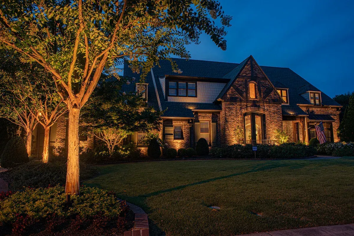 A landscaped garden bed with decorative rocks, small shrubs, and glowing orb lights against a wooden fence at dusk.