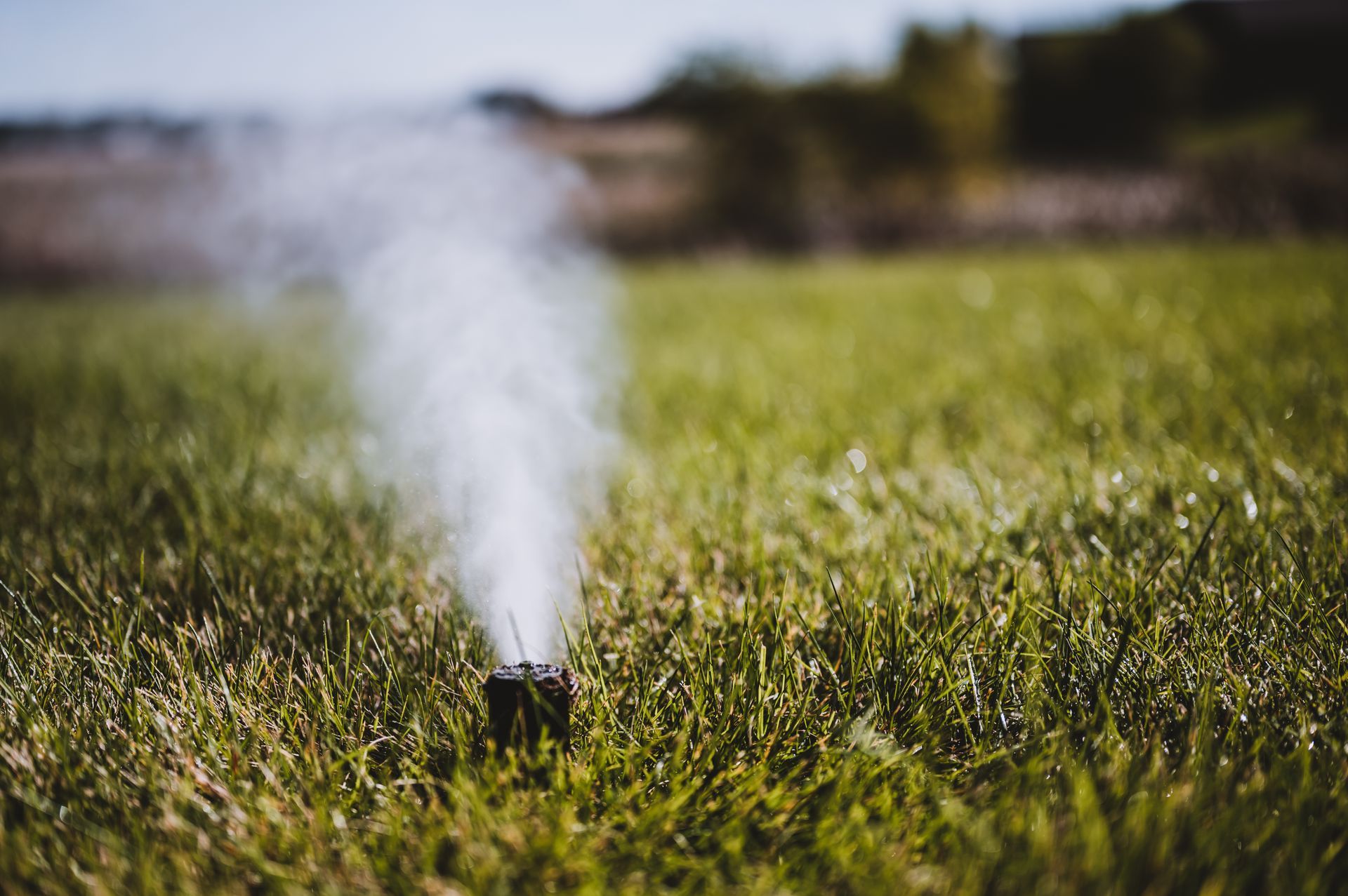 A lawn sprinkler spraying a fine mist into the air over a green, grassy field on a sunny day.