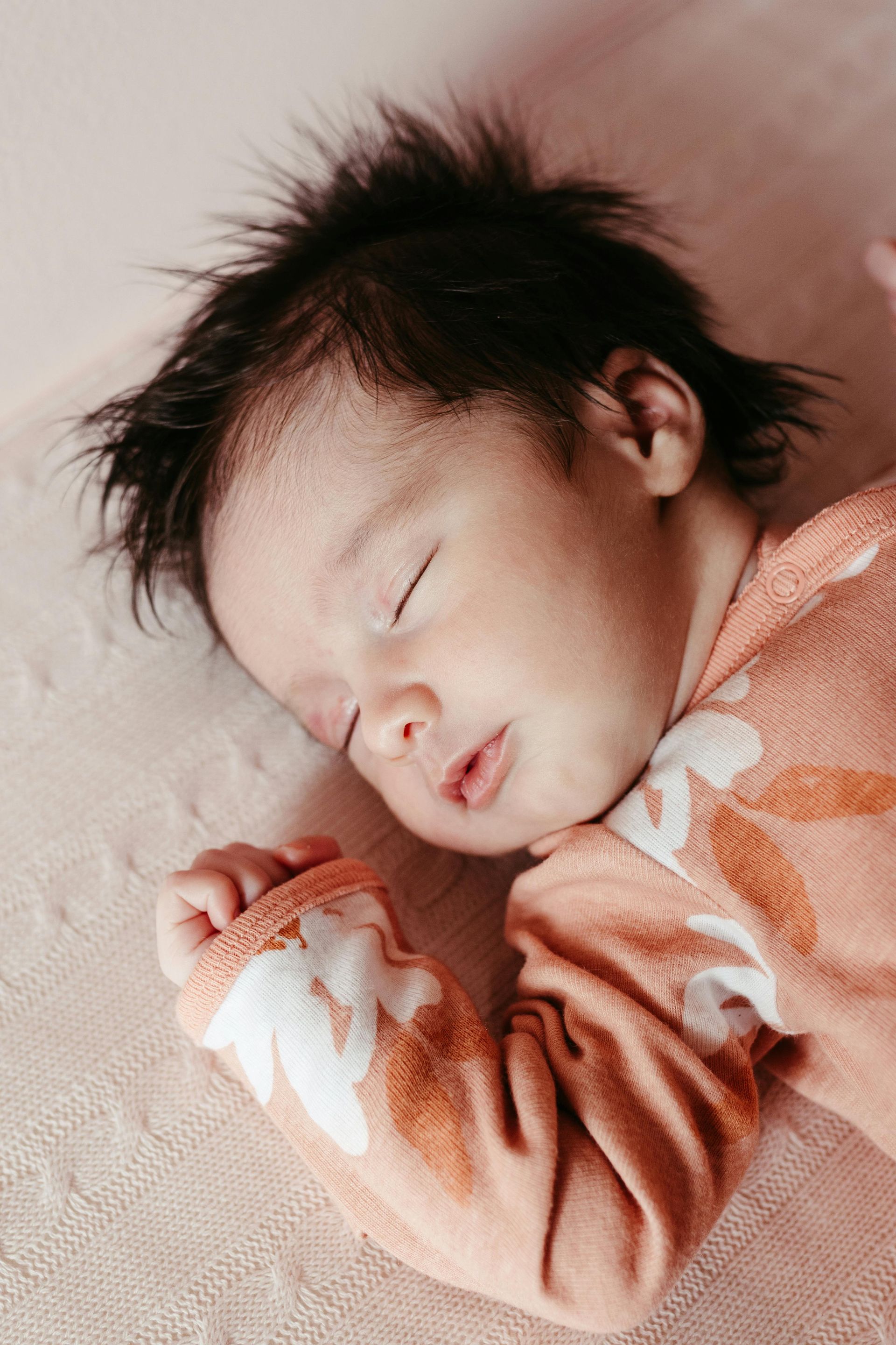 A baby is sleeping on a pink blanket on a bed.