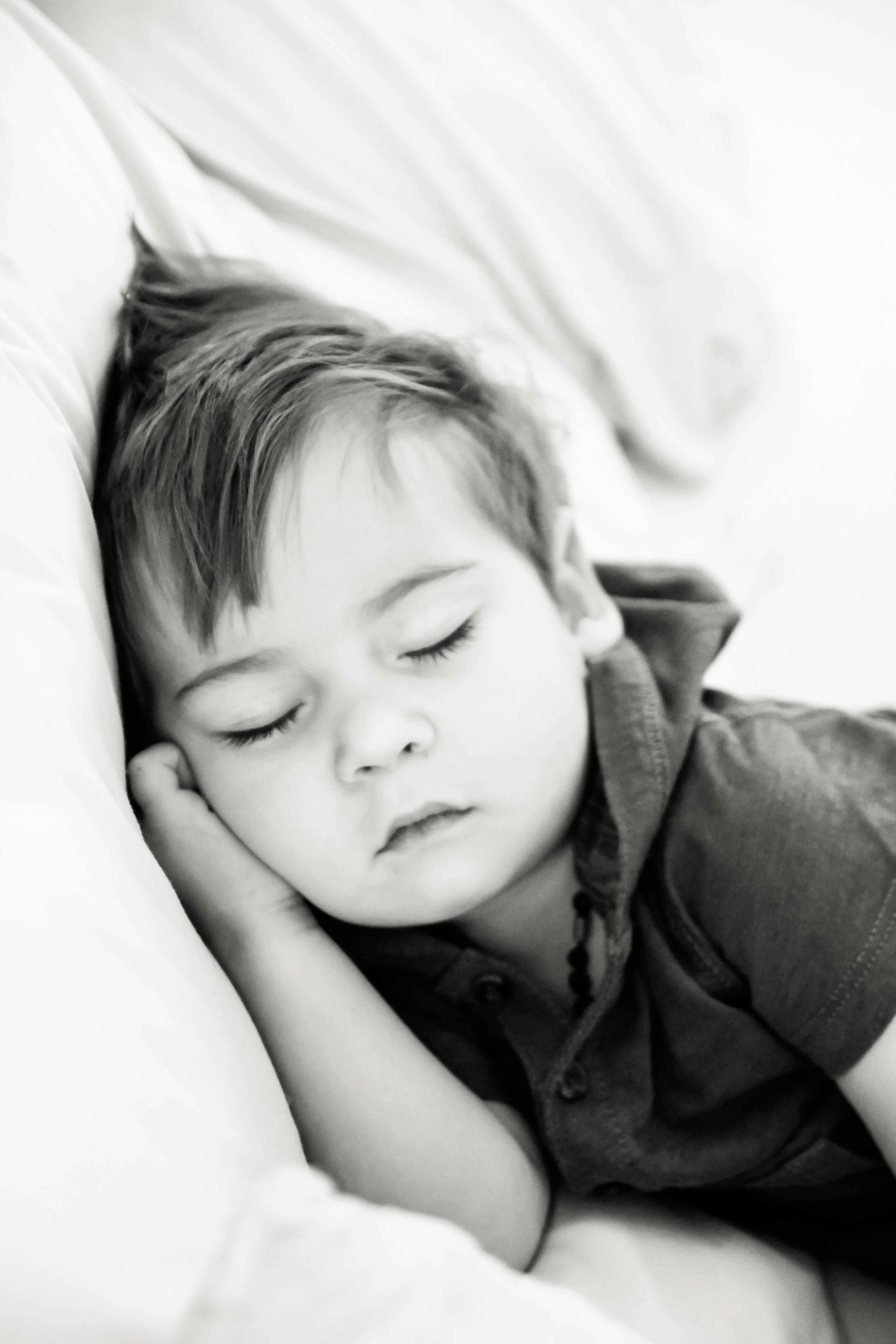 A black and white photo of a young boy sleeping on a bed