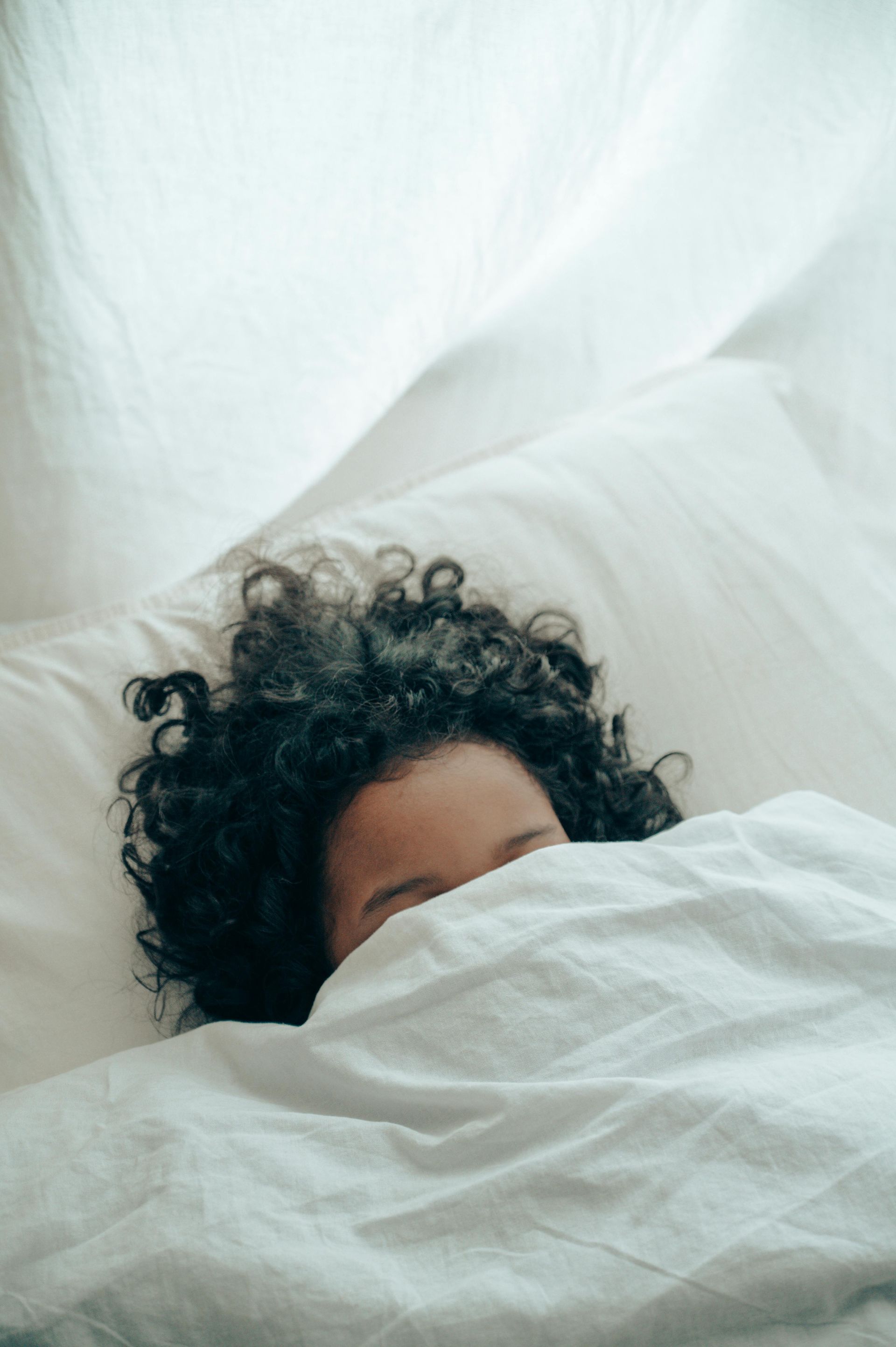 A woman with curly hair is laying in bed under a white blanket.