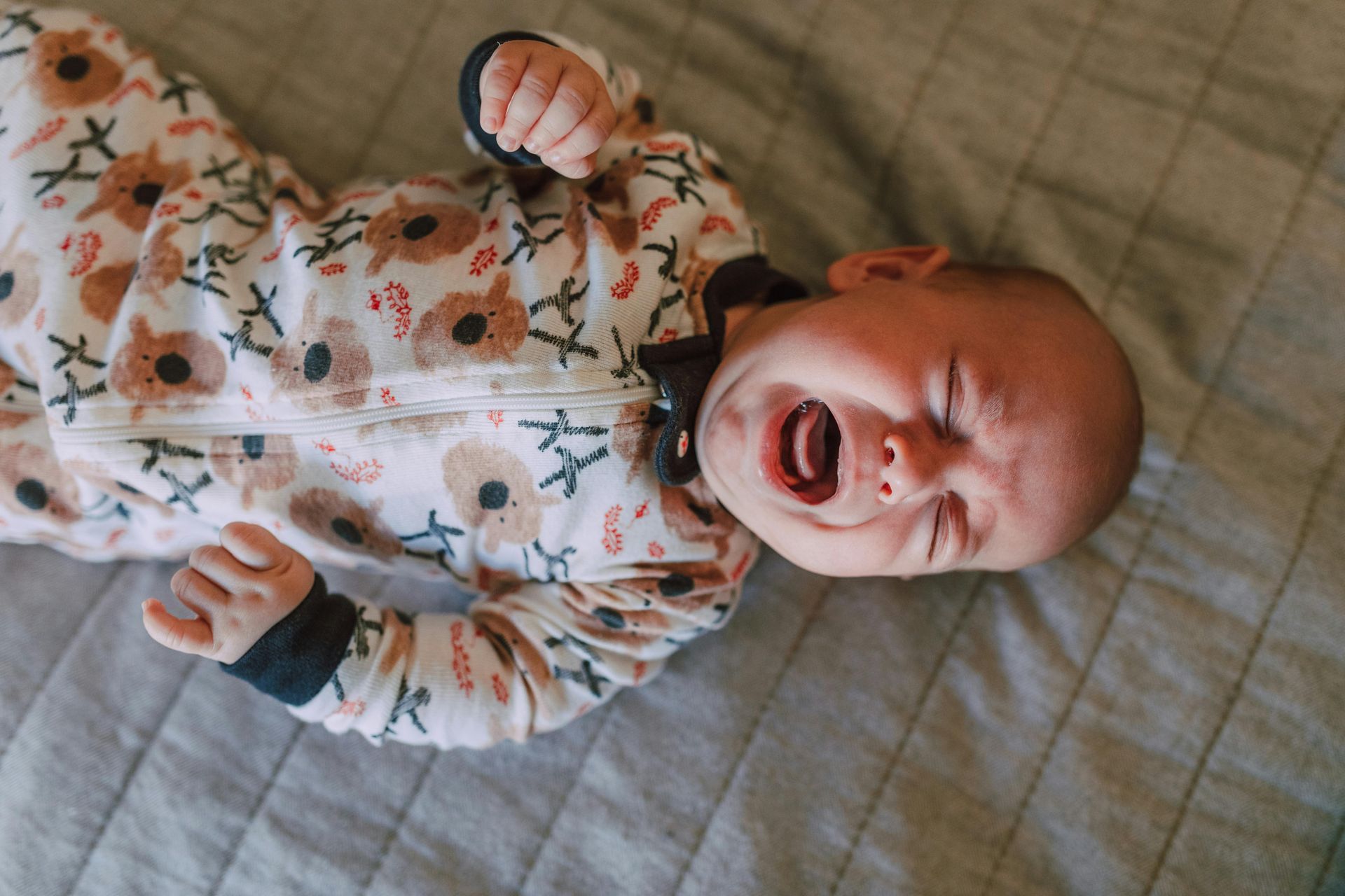 A baby is crying while laying on a bed.